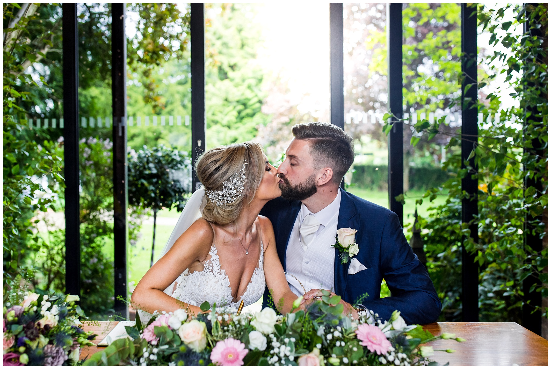 bride and groom kiss in front of ceiling high windows and open gardens at redhouse barn