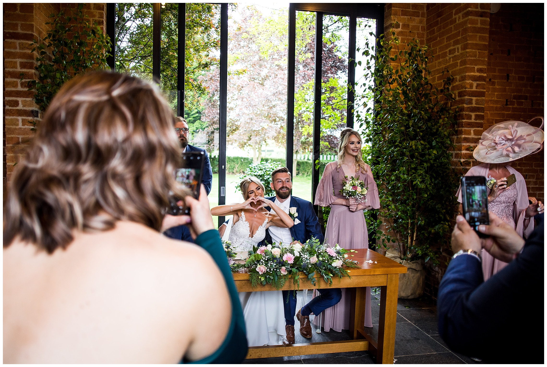 wedding guests taking photos of bride and groom making heart shape with hands