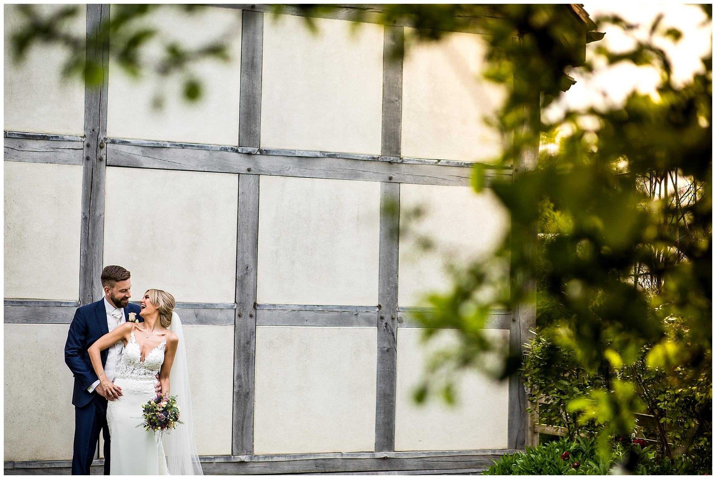 bride and groom holding onto one another laughing in front of barn venue