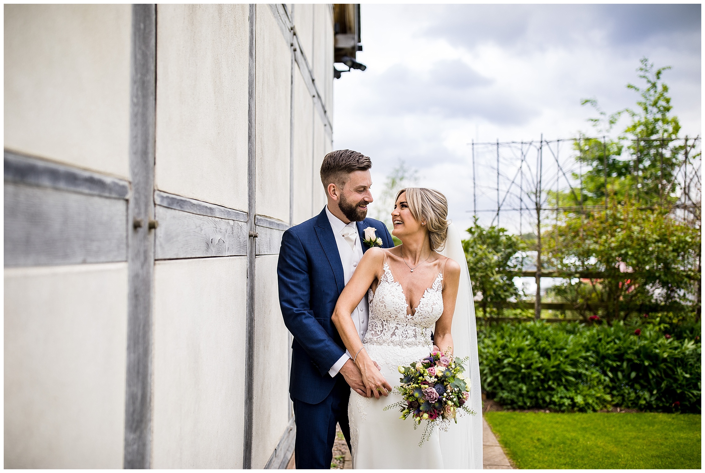 bride and groom stand together smiling at each other in front of redhouse barn