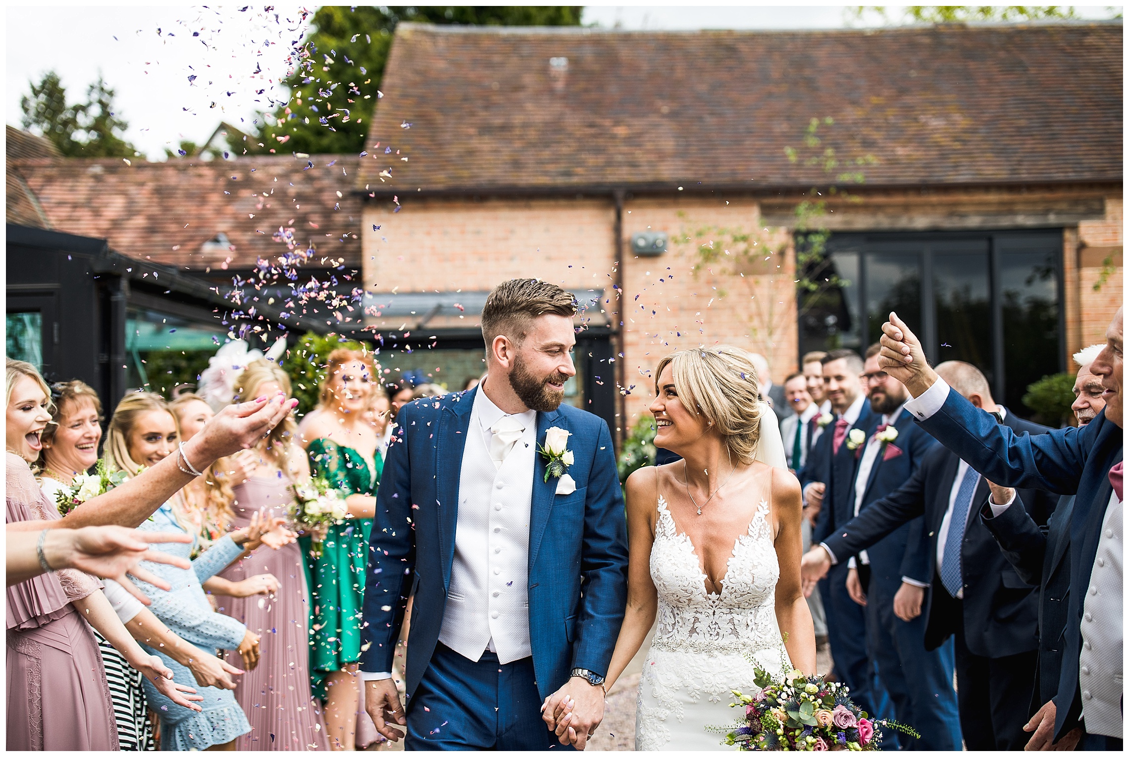 bride and groom looking at one another as guests look on and throw petal confetti at them
