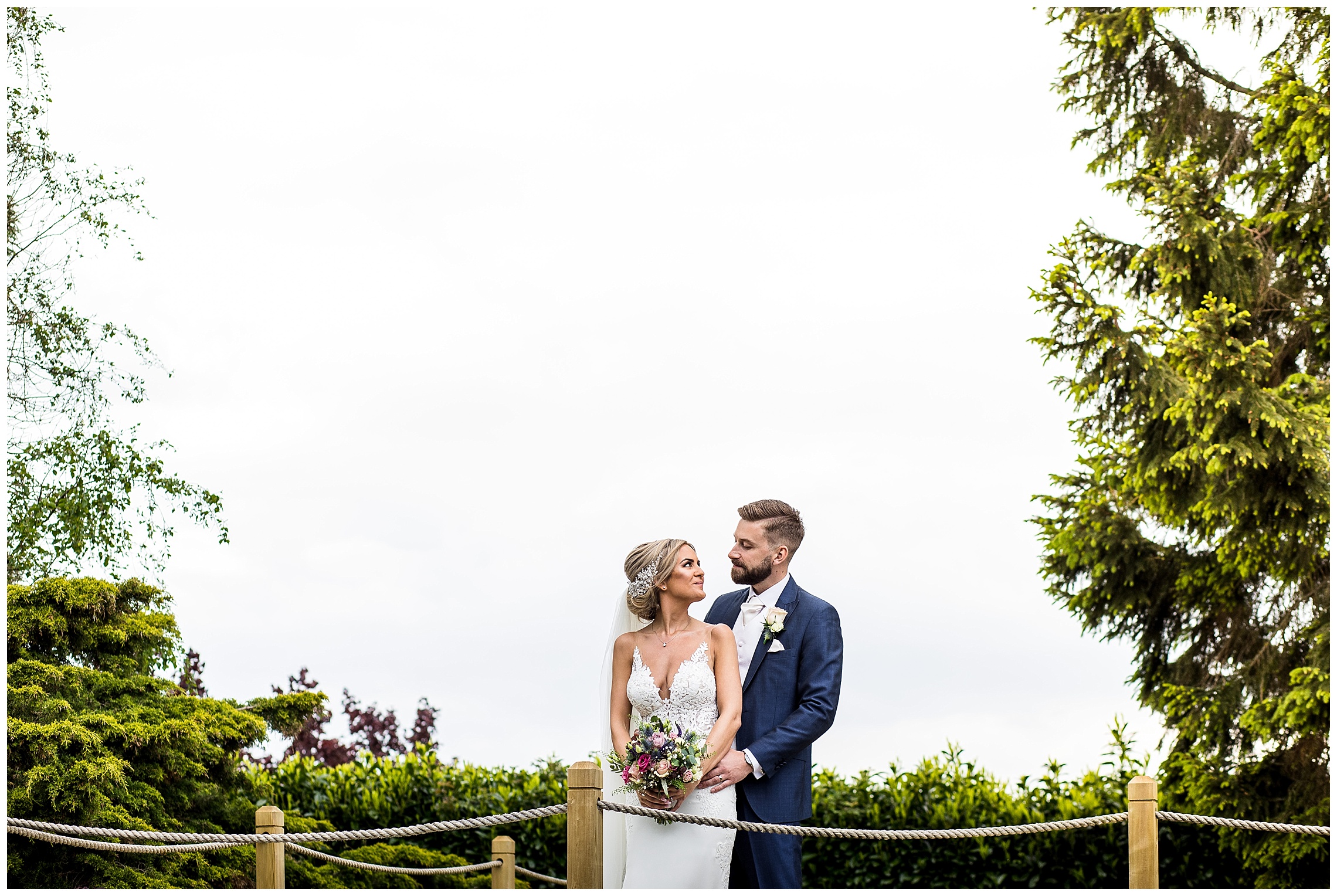 bride and groom between trees over lake