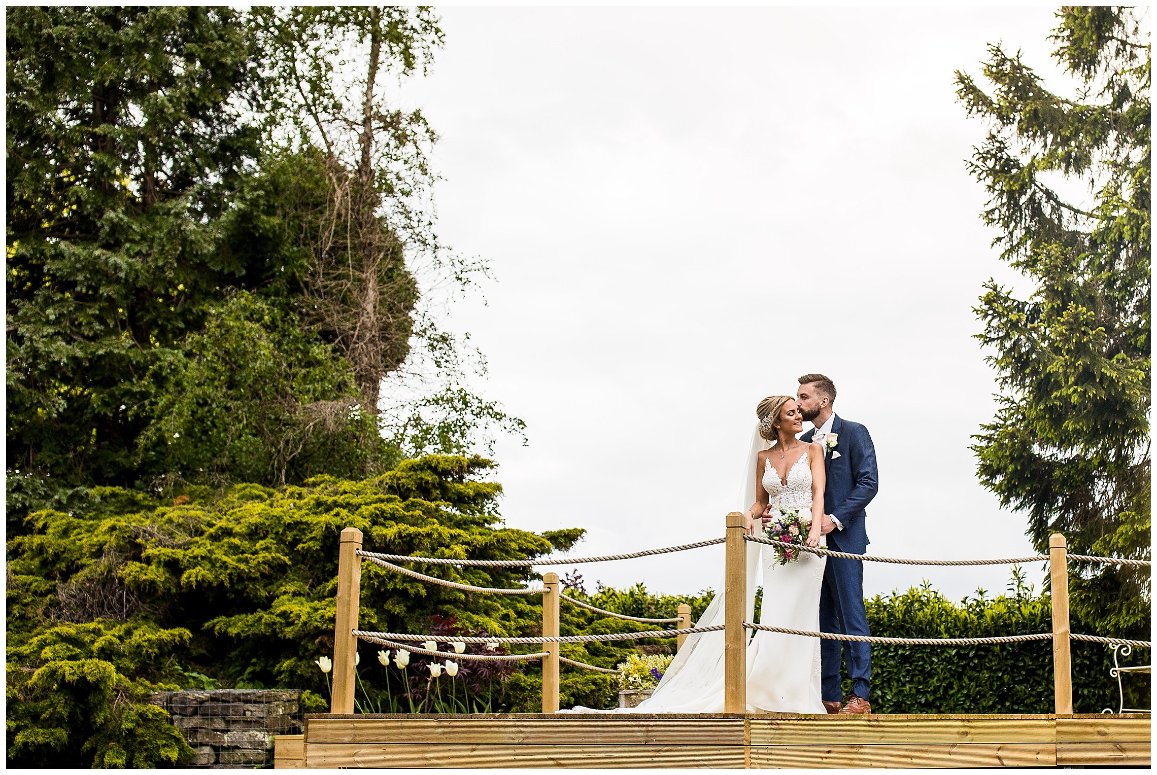 bride and groom kissing on bridge over lake