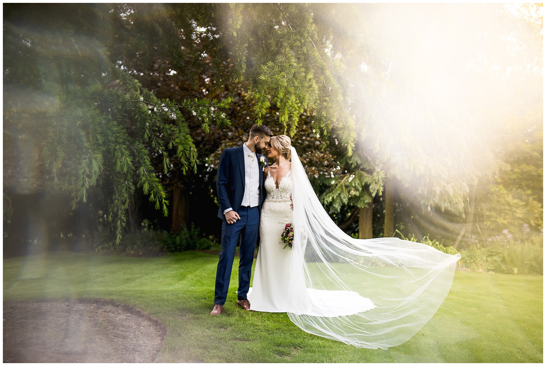 bride and groom stand together with heads resting together and veil flowing in wind