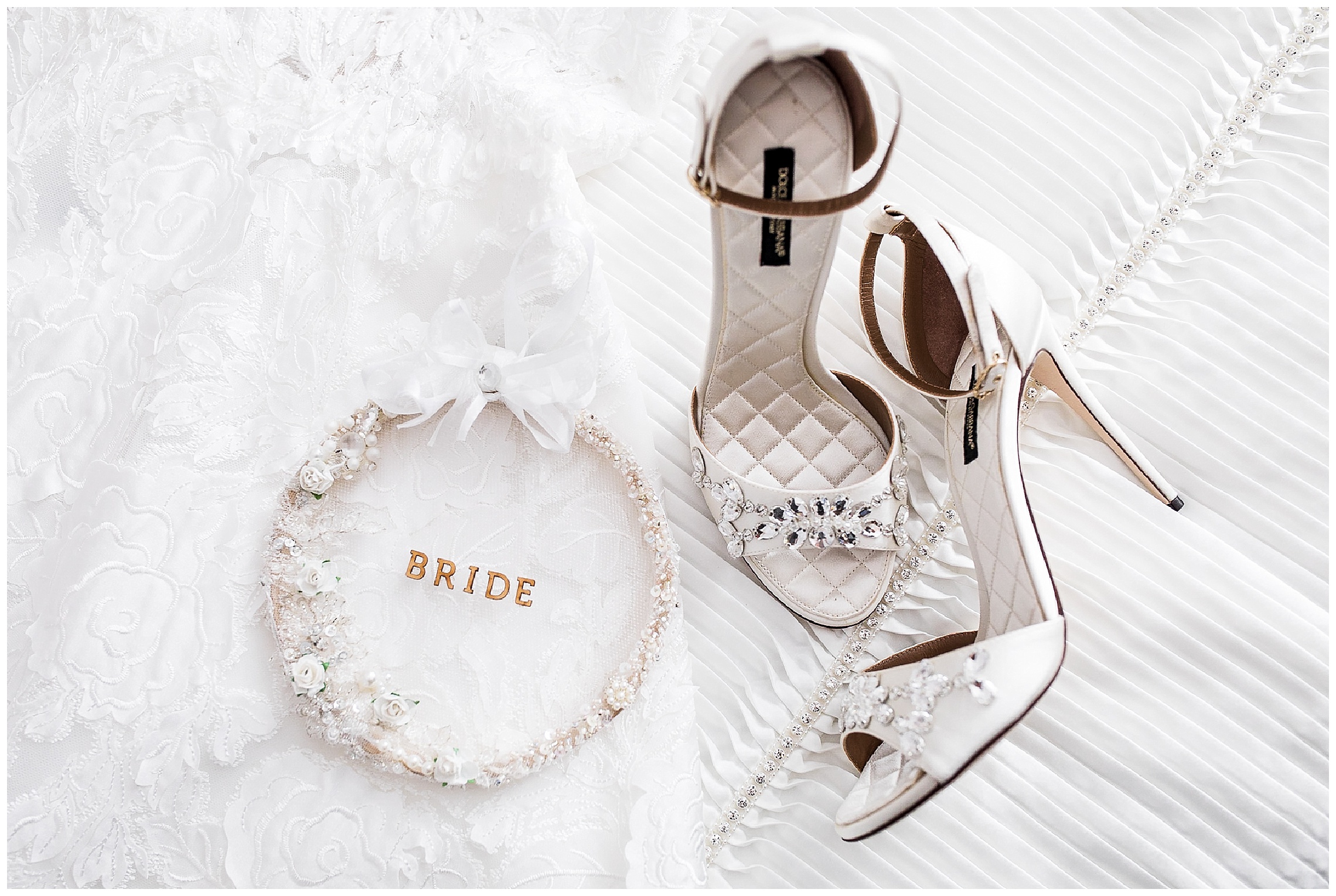 white dolce and gabbana bridal shoes with straps and diamanté details, on a while bed next to a bride decoration
