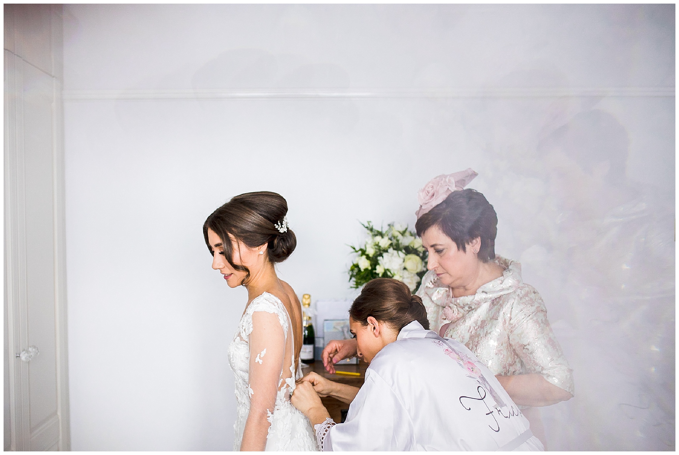 bride with hair up stood in bedroom as mum does up long sleeved wedding dress