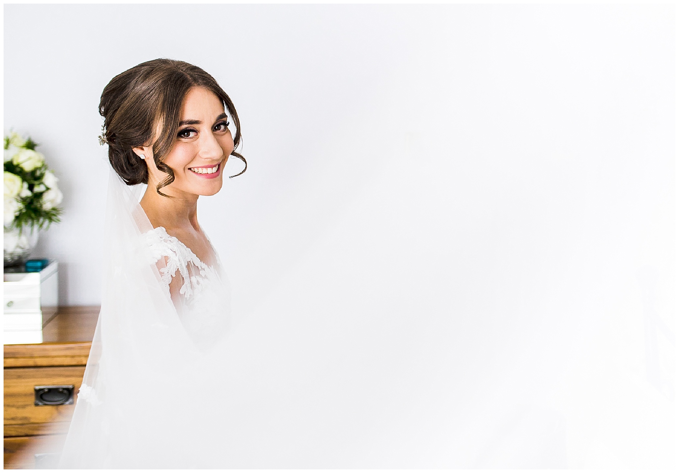 bride with long veil looking over shoulder and smiling as brown curly hair frames her face