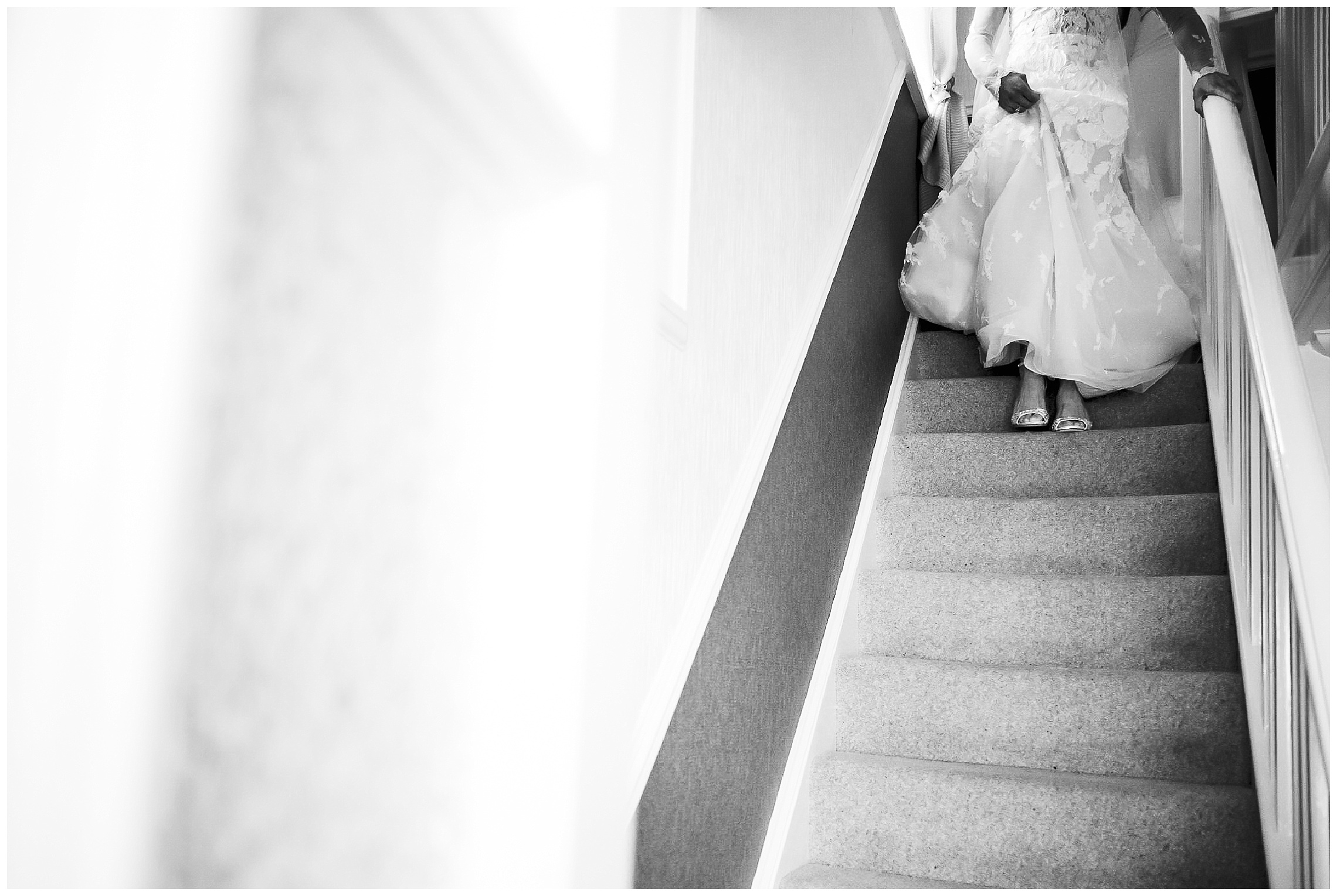 black and white image of bottom half of wedding dress and hands on bannister as bride descends staircase