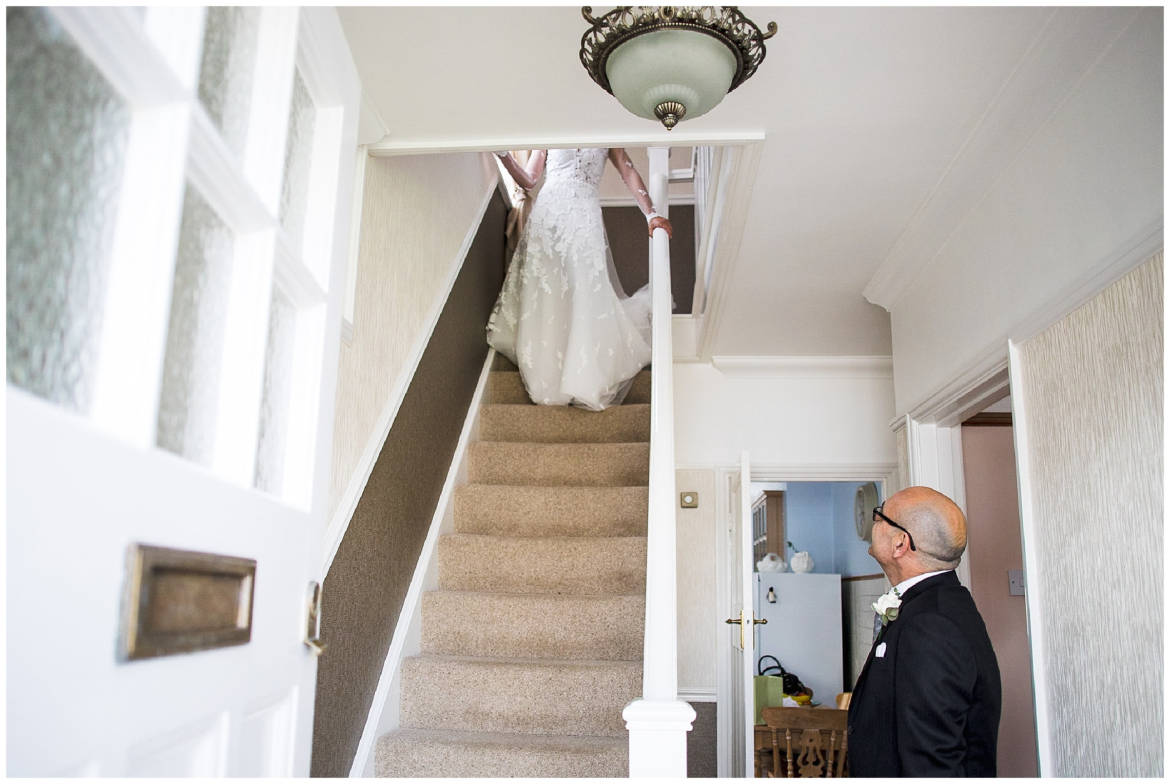 father of the bride watching bride come down stairs in white wedding dress
