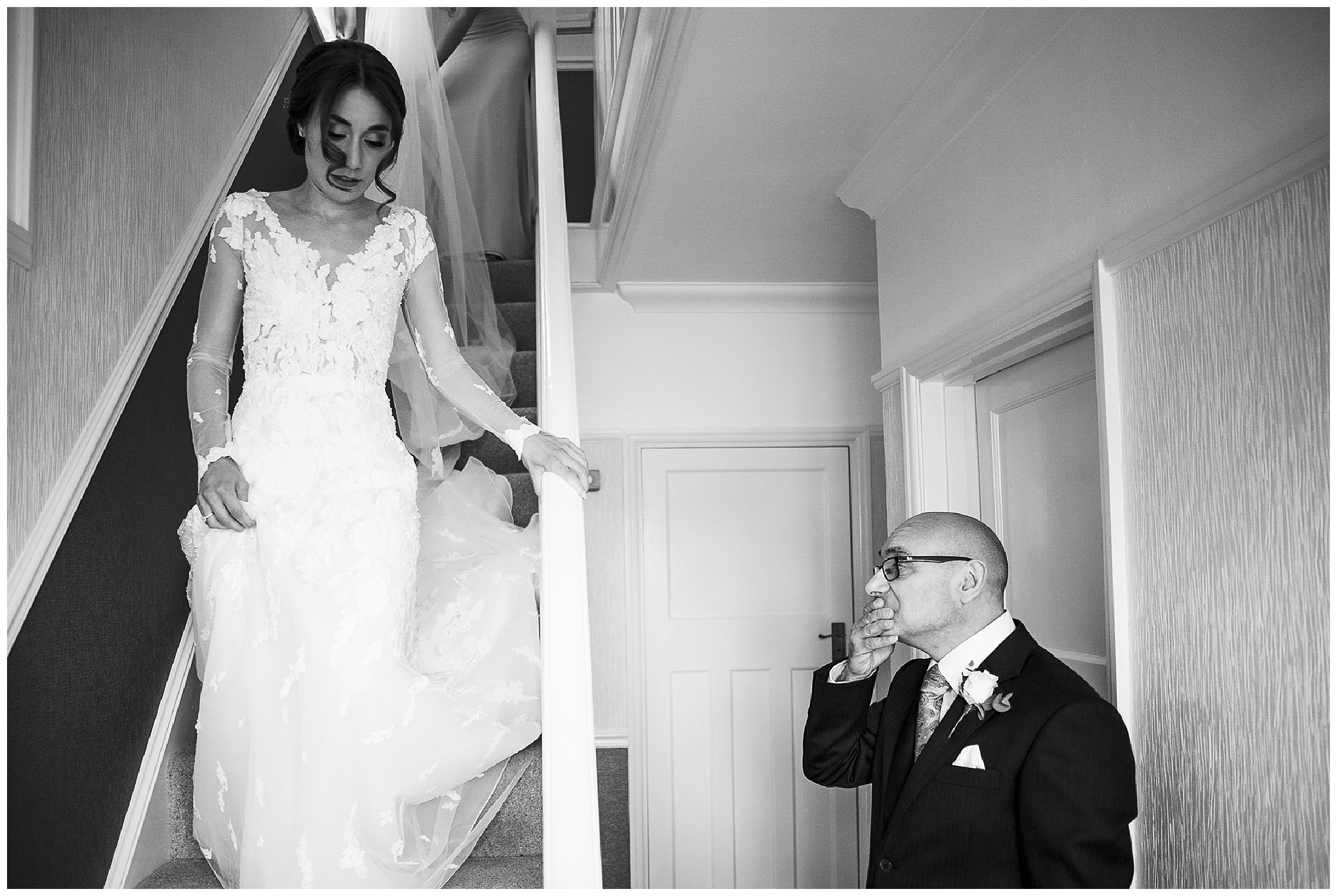 father of the bride rubbing his mouth nervously as bride descends stairs