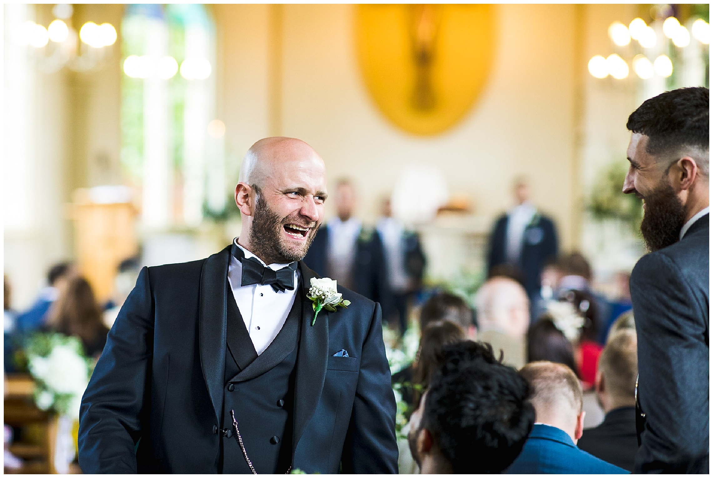 groom laughing at end of aisle, in bow tie and tuxedo suit