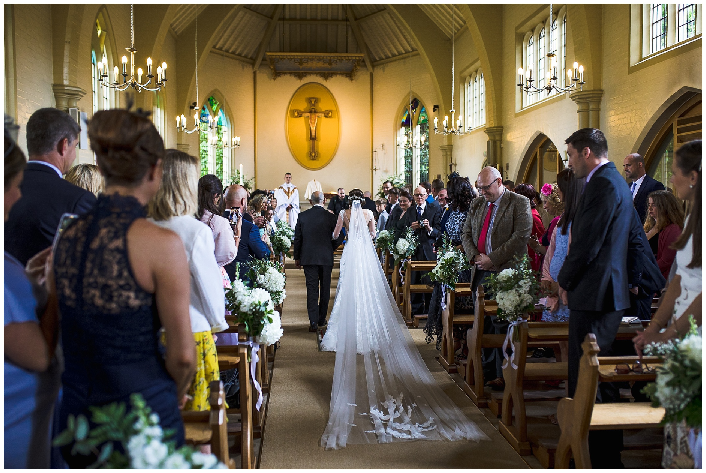 bride with long veil walks down aisle in catholic church with dad