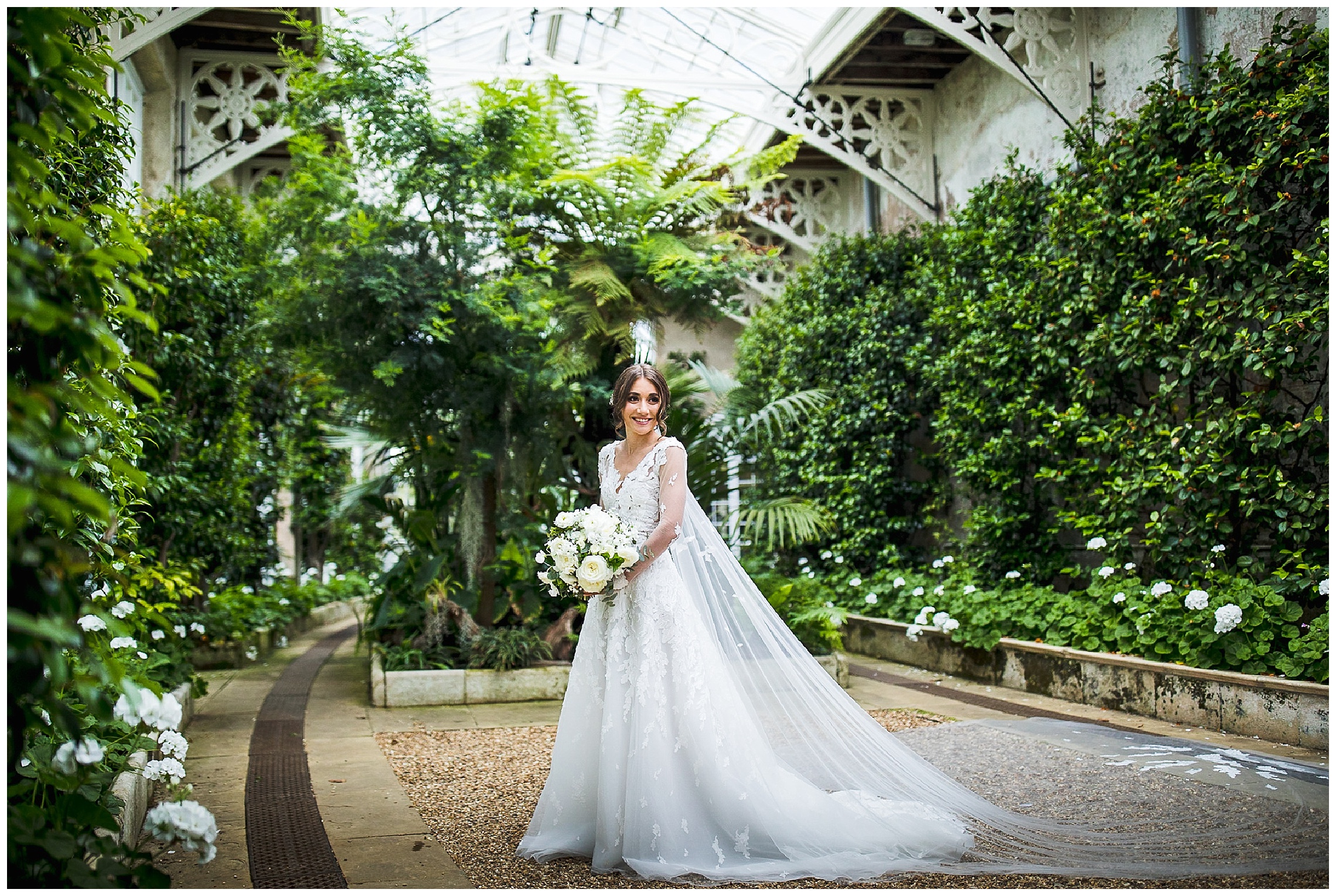 bride in long sleeved dress and long veil stood with white flowers in camellia house at woburn sculpture gallery