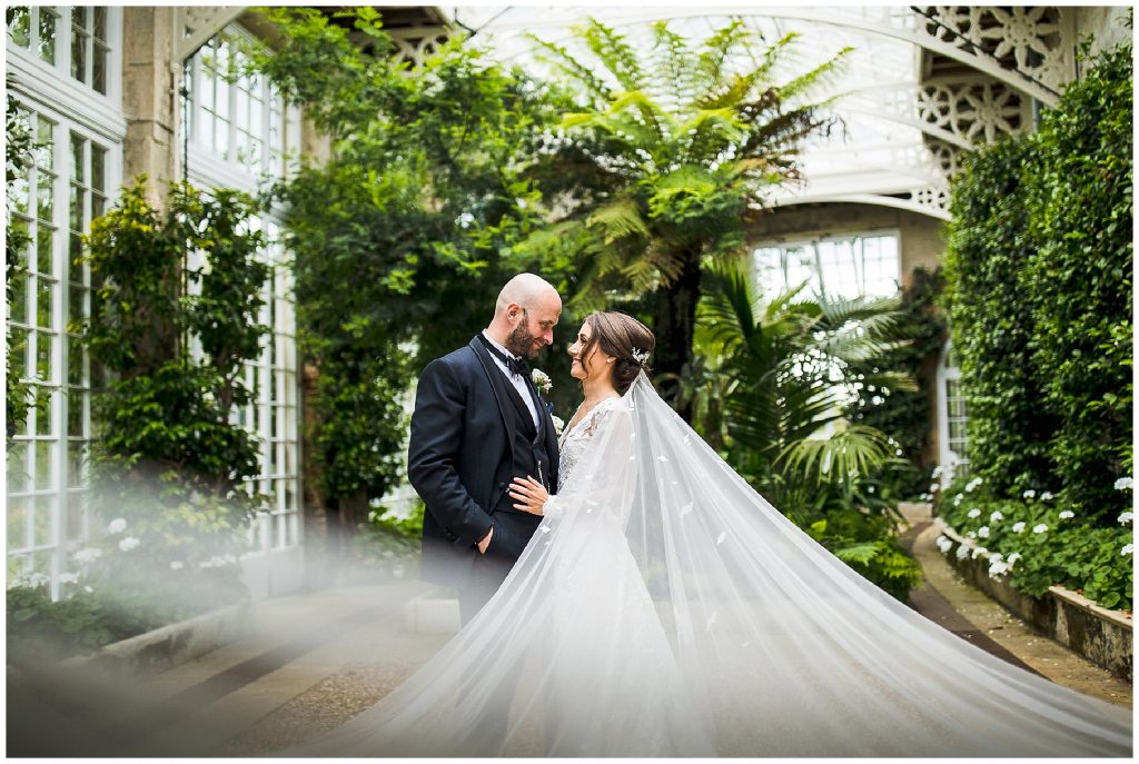 bride and groom look into each others eyes as veil blows in wind