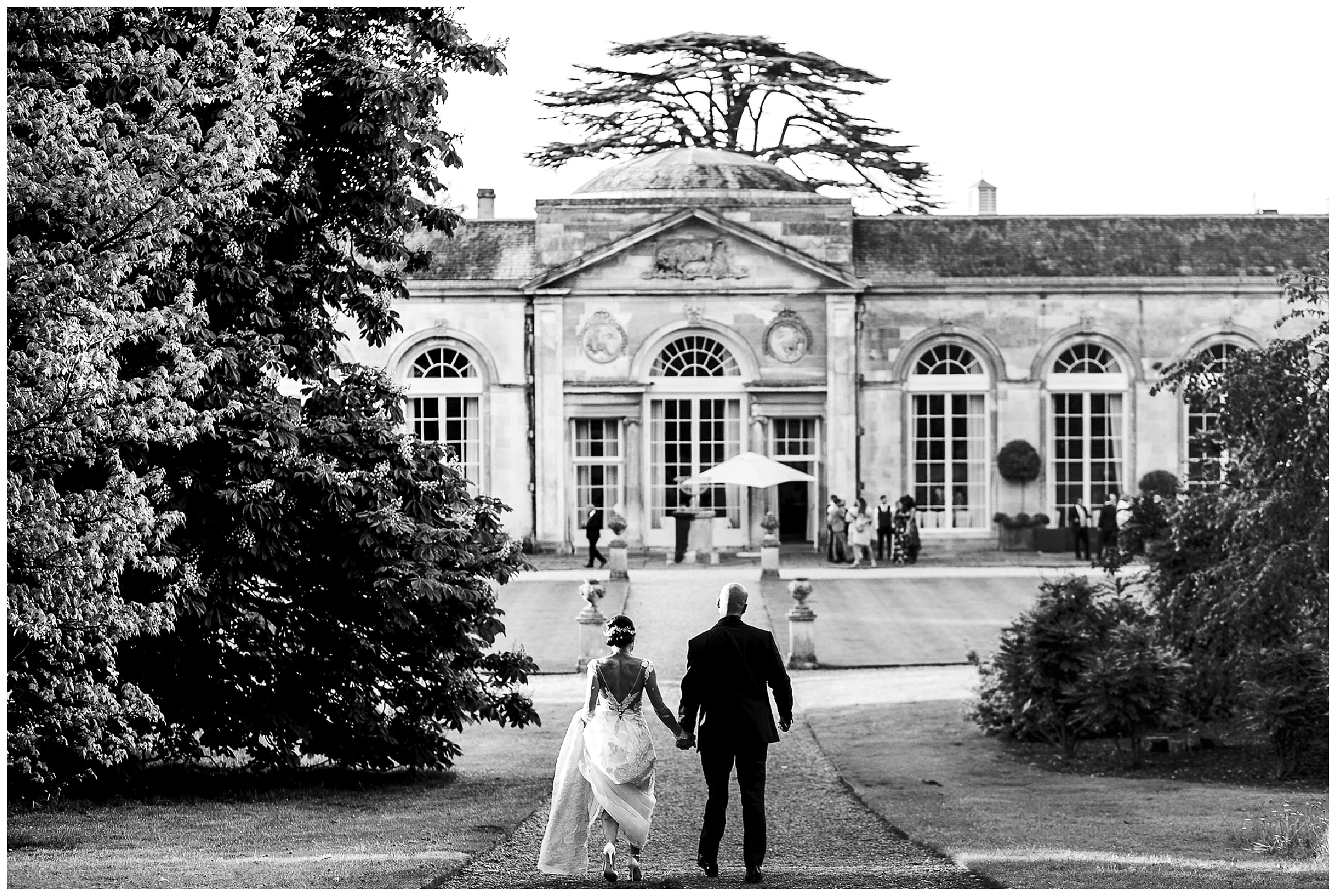 black and white image of bride and groom walking hand in hand, the bride is scooping her dress up into her arms