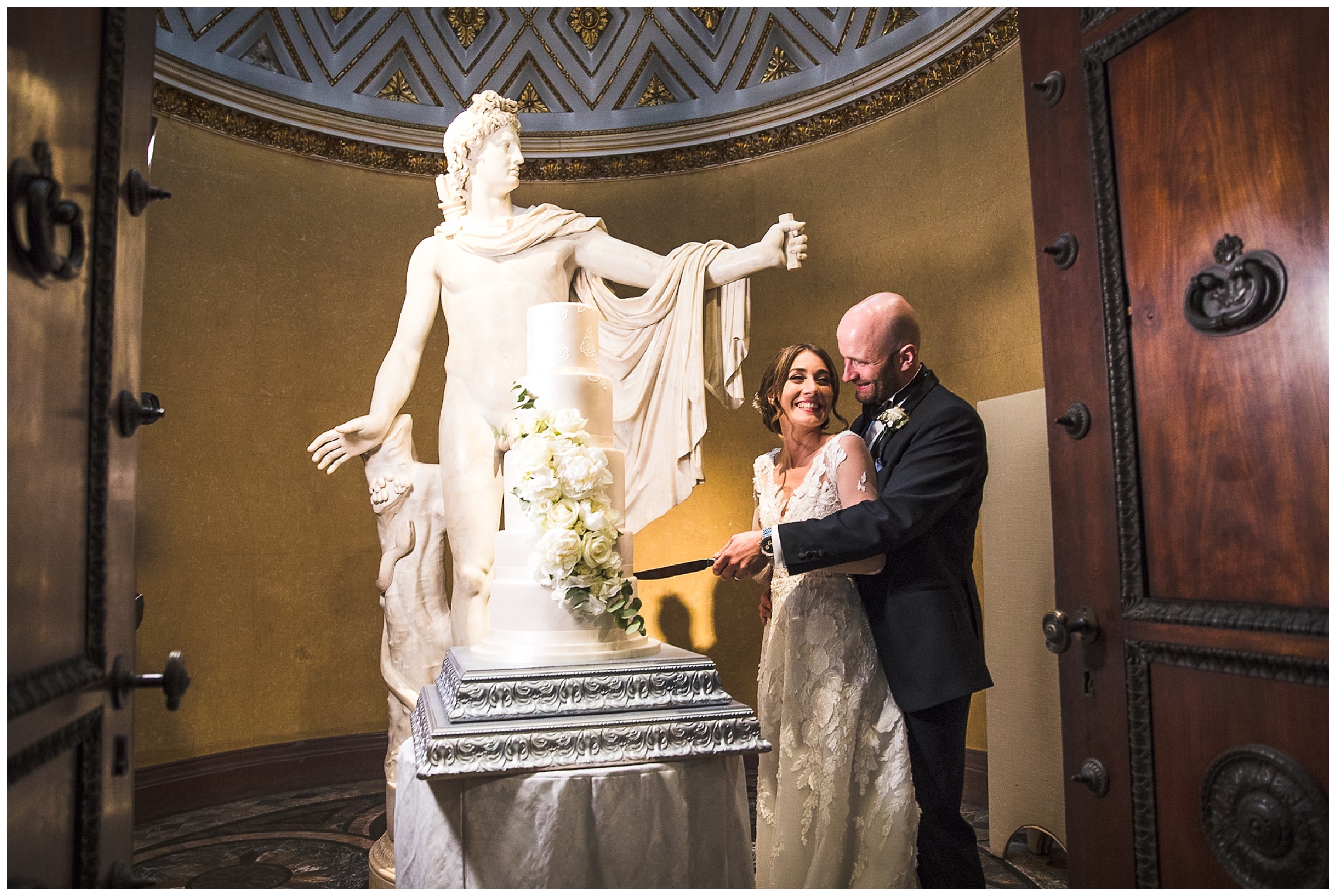bride and groom cut tiered cake in front of david of apollo statue