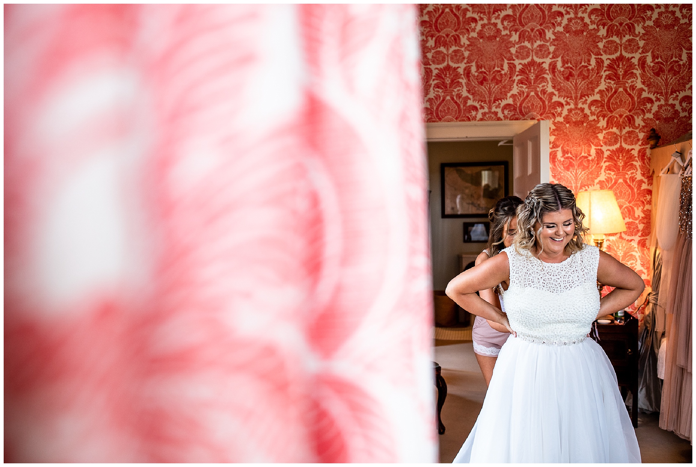 bride having her dress done up by bridesmaid stood behind her