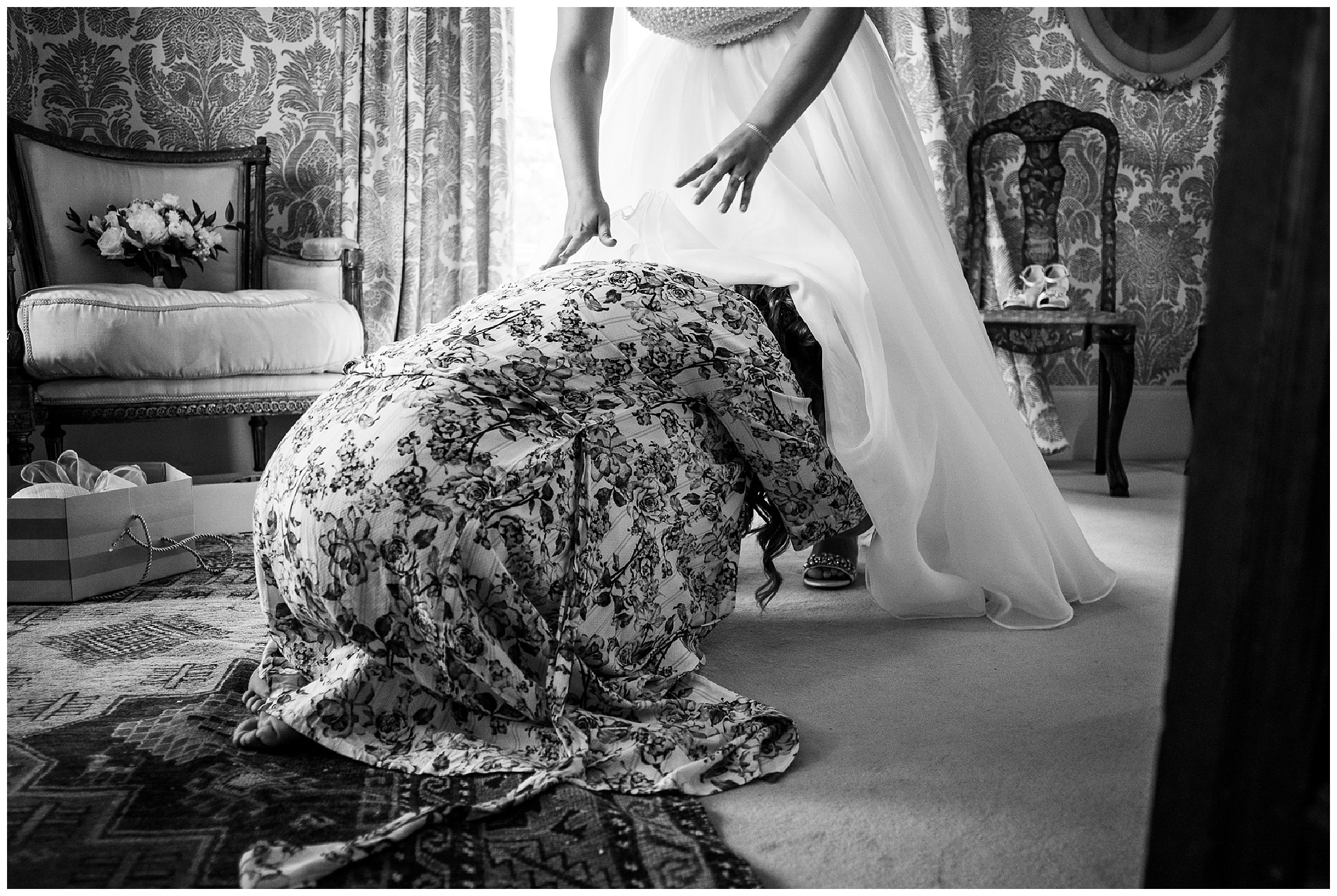 bride leaning forward onto bridesmaid who is helping put shoes on