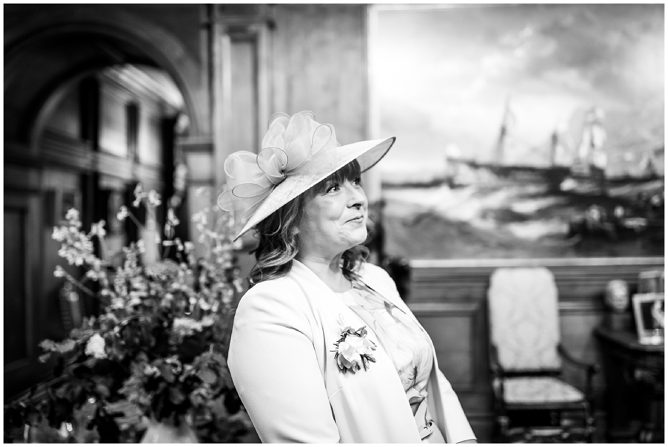 step-mother of the bride in wide brimmed hat looks on as bride descends stairs and cries