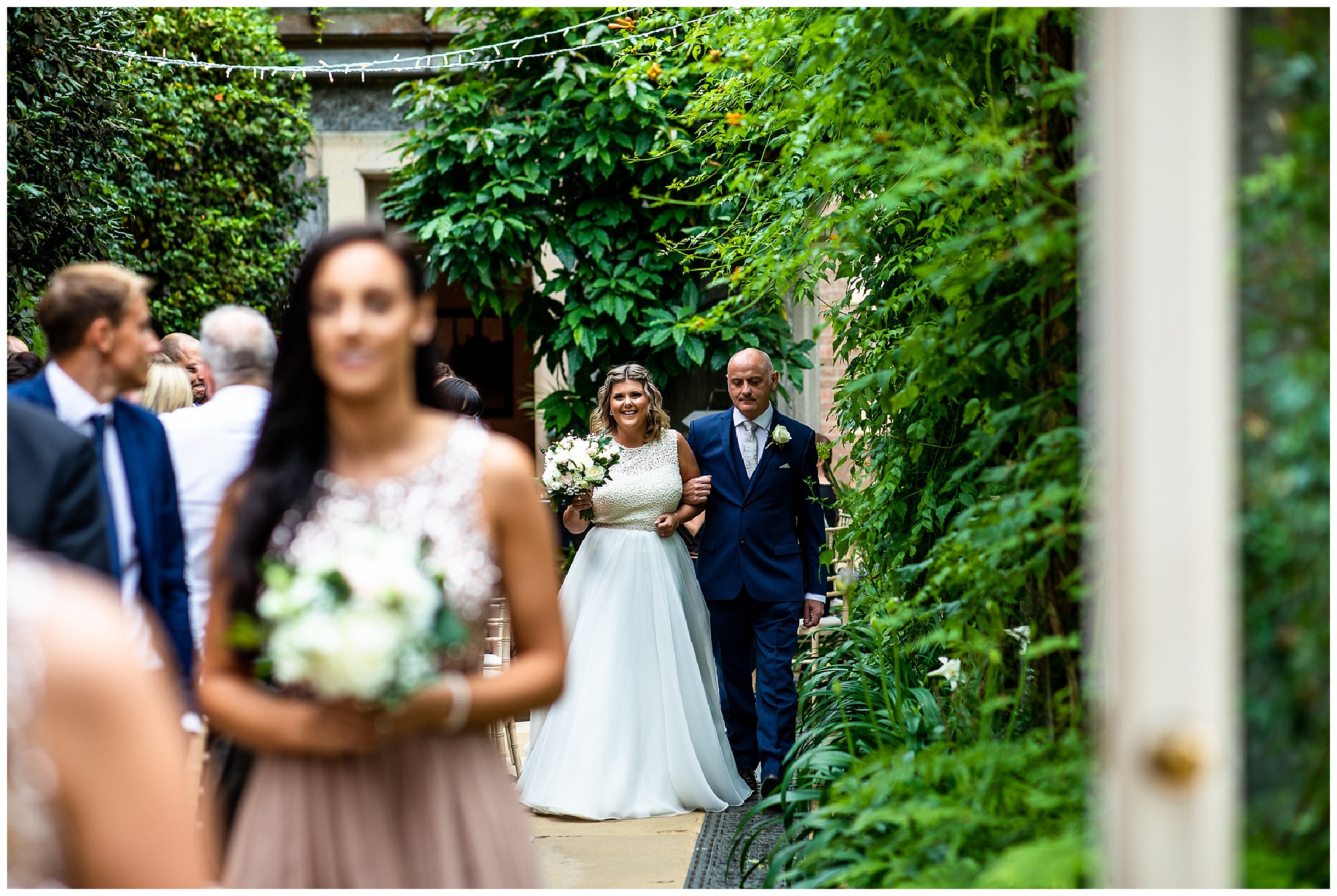 bride enters ceremony room smiling whilst her father looks at floor