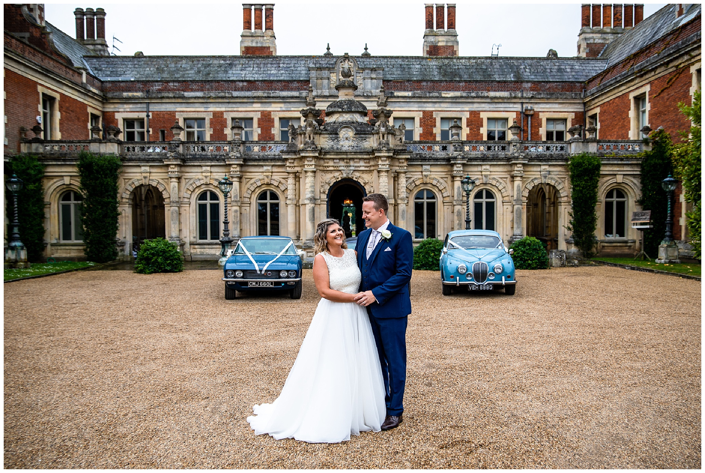 bride and groom holding hands in front of blue wedding cars outside large brick venue somerleyton hall
