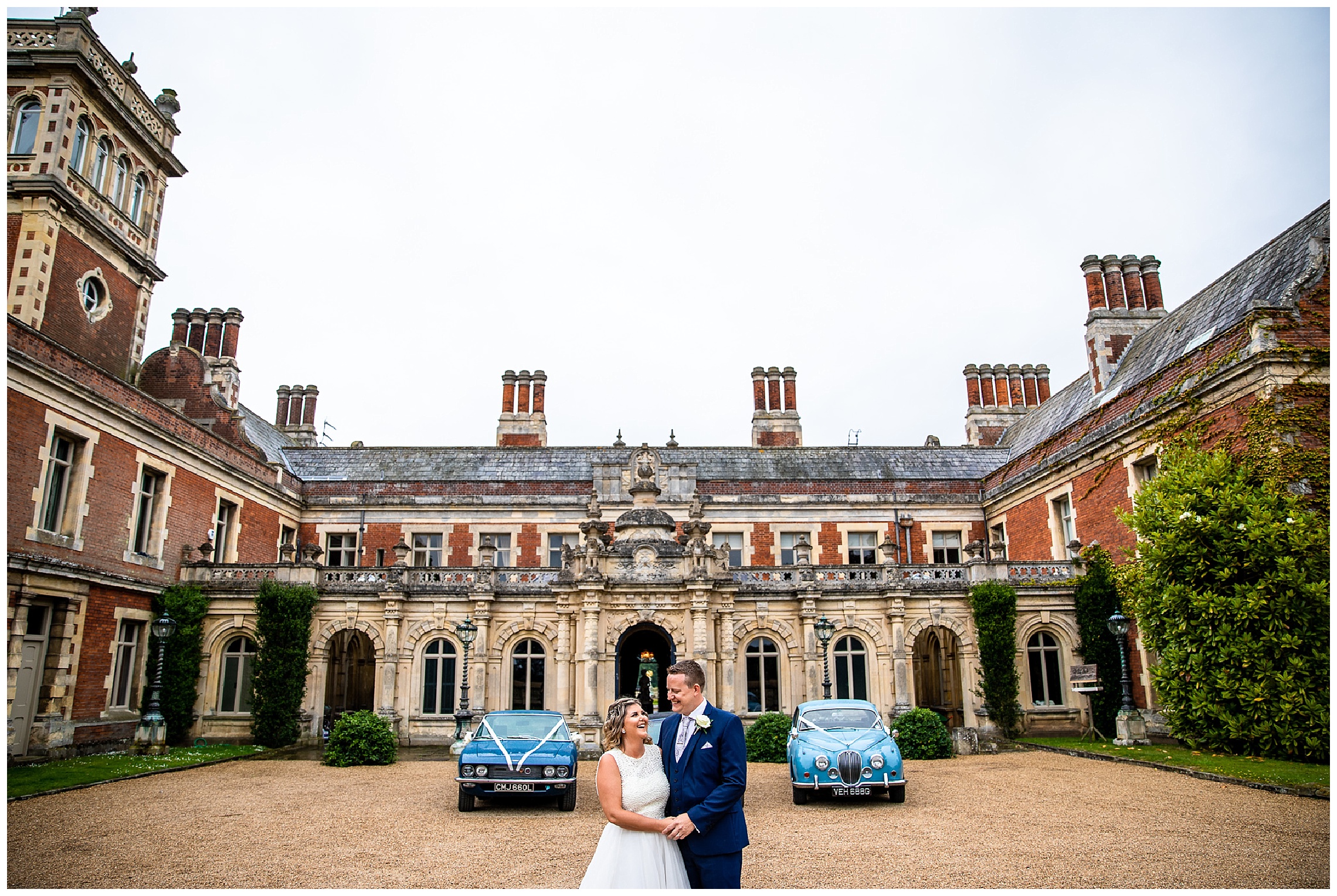bride and groom stand in front of blue wedding cars