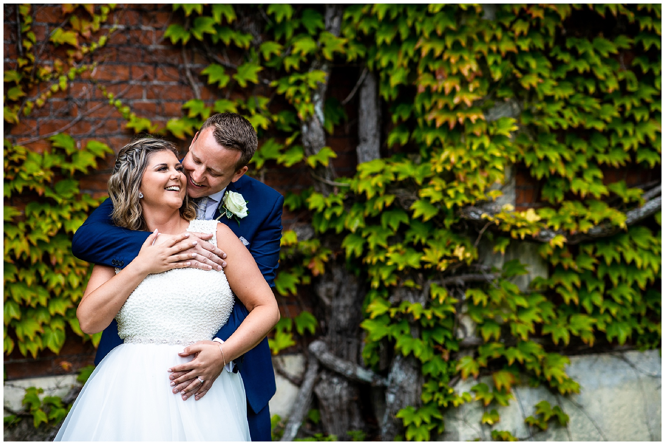 bride and groom cuddle and laugh in front of wall of ivy at somerleyton