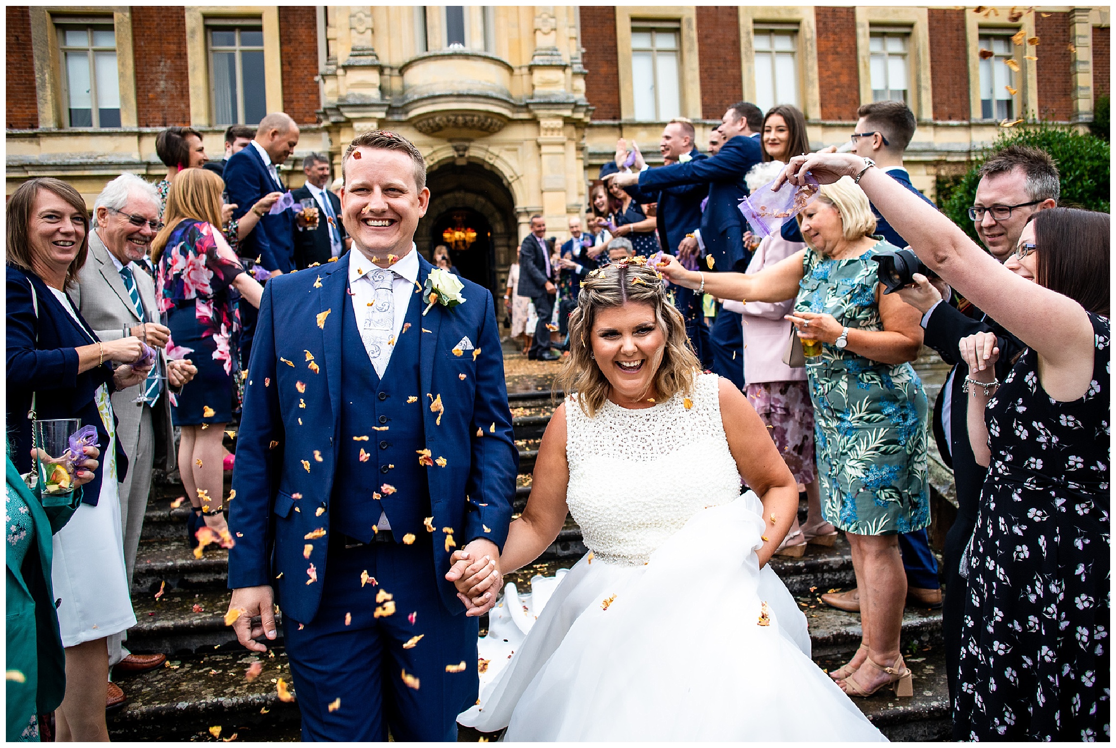 bride and groom descend steps of somerleyton hall as natural confetti is thrown over them