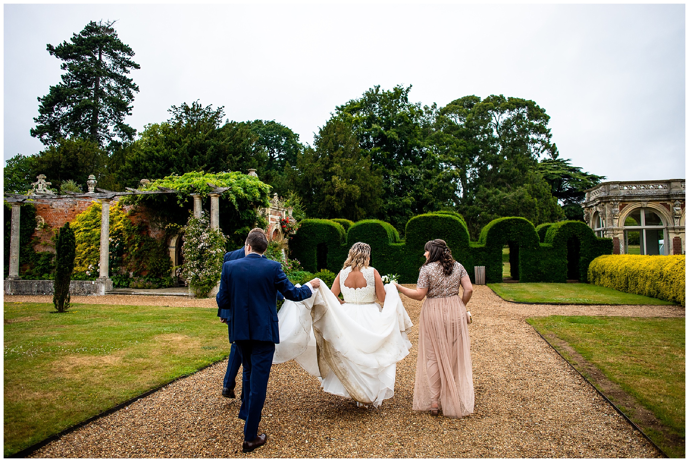 bride walking with dress held up by groom and bridesmaid at somerleyton hall