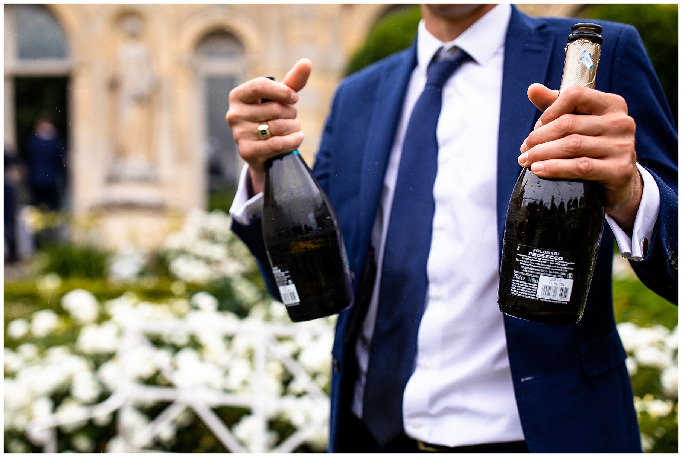 wedding guest in suit holding onto two bottles of champagne