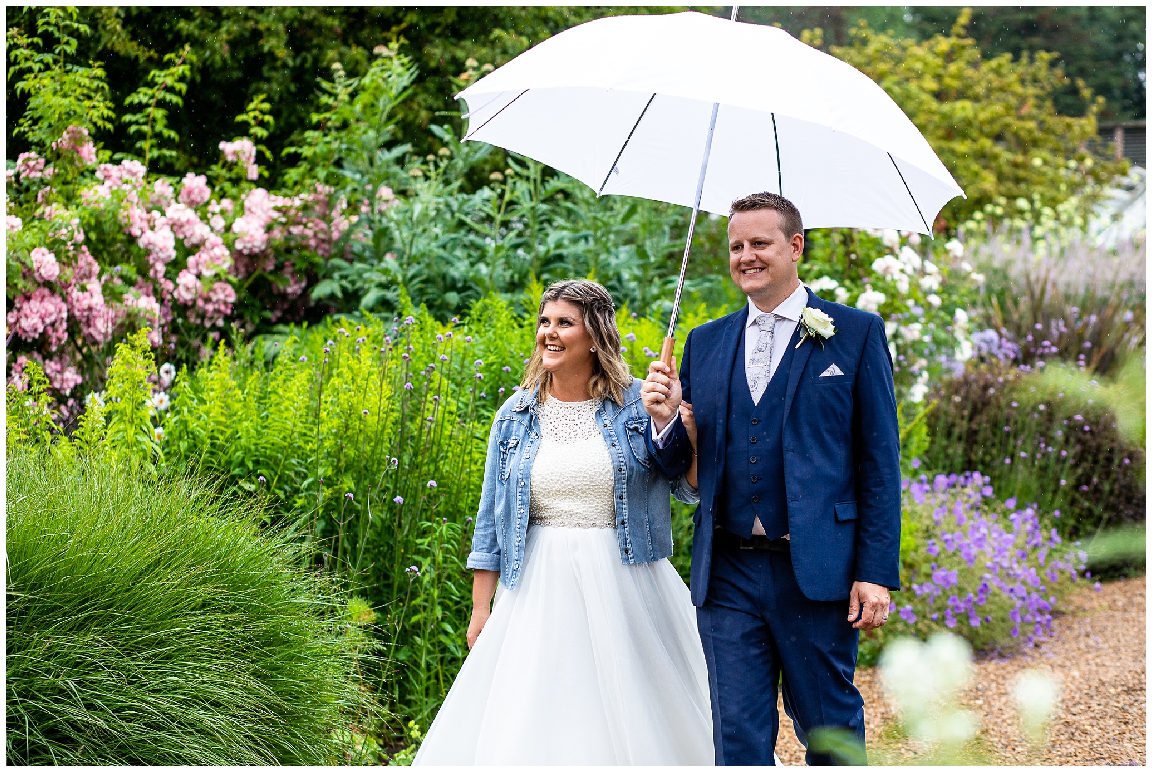 bride and groom walking through gardens of someleyton hall with umbrella in the rain