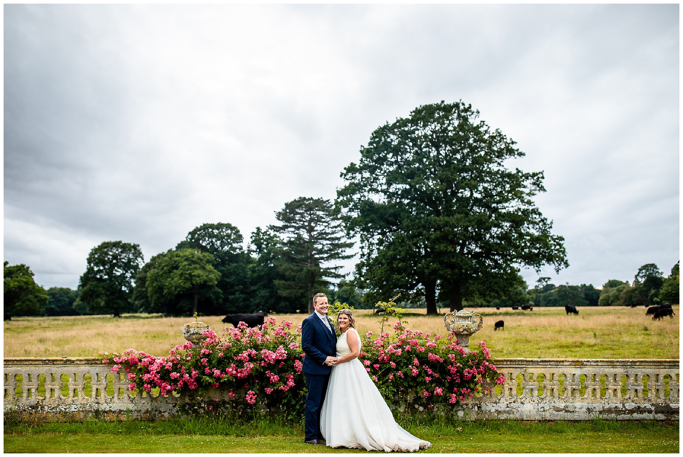 bride and groom stood in front of fields with dark moody sky and bright pink flowers