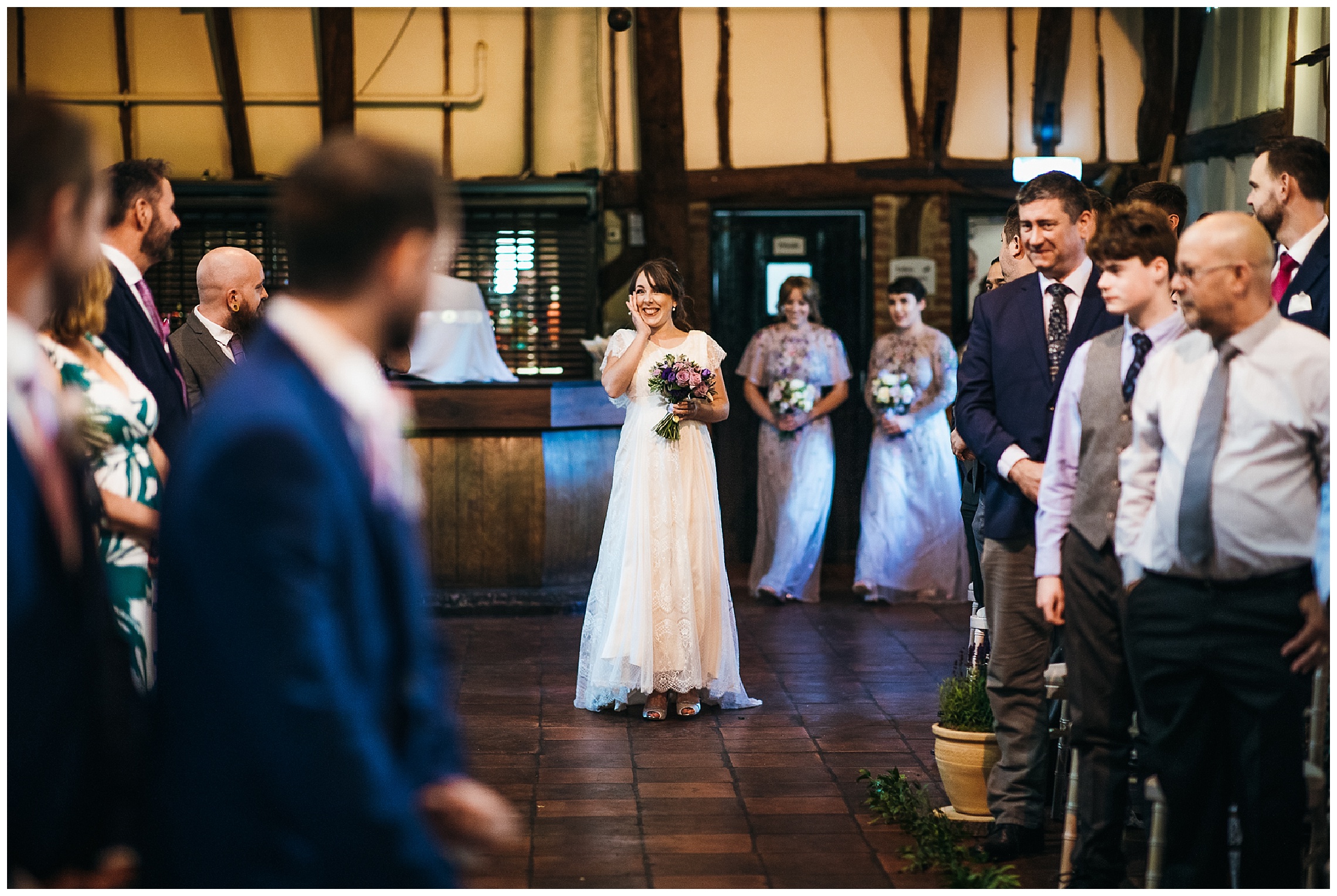 bride walks towards groom smiling with hand up to her face in barn venue