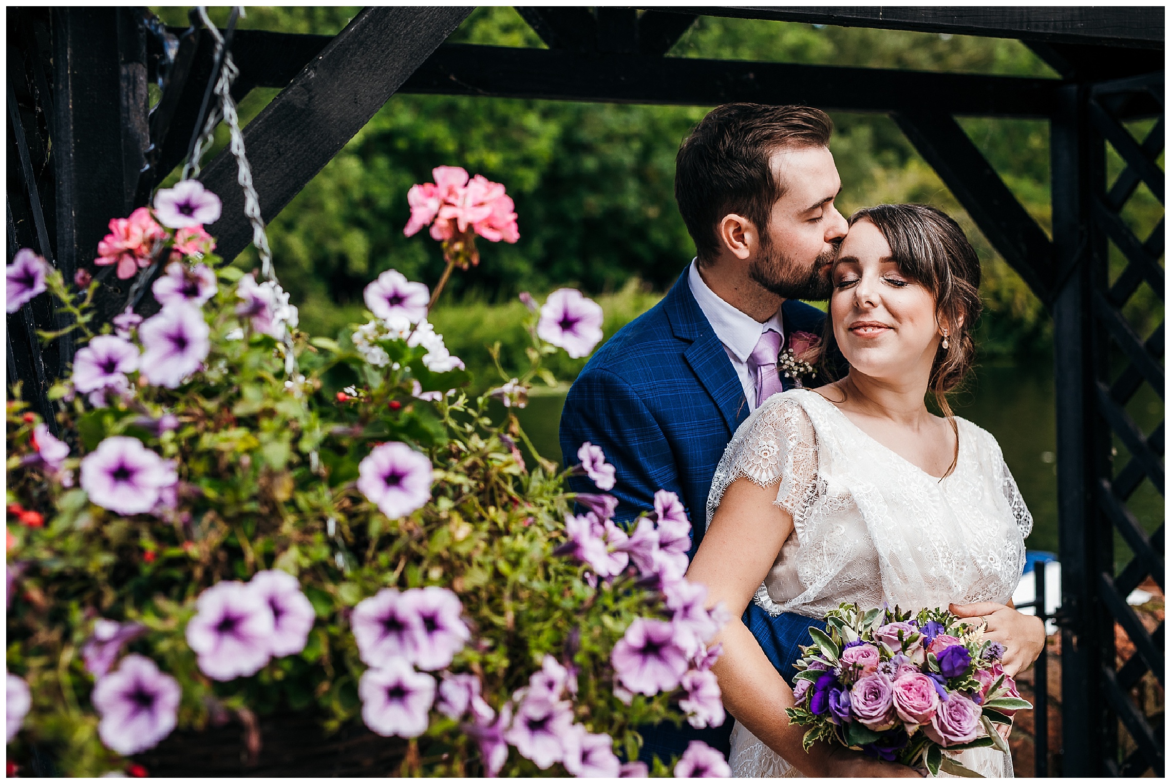 groom kissing pregnant bride on forehead with pansies in foreground