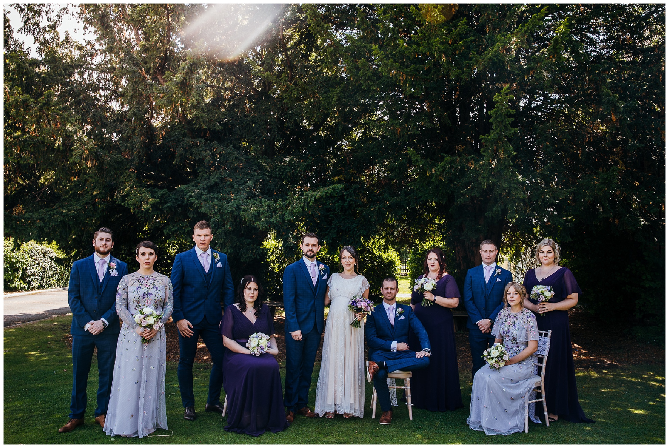 group shot of bridesmaids in purple dresses standing and sitting with groomsmen also at barns
