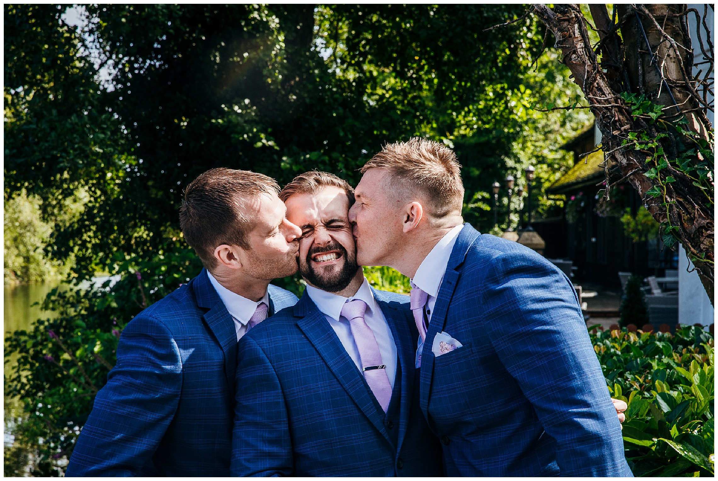 groom being kissed on cheek by groomsmen in blue suits
