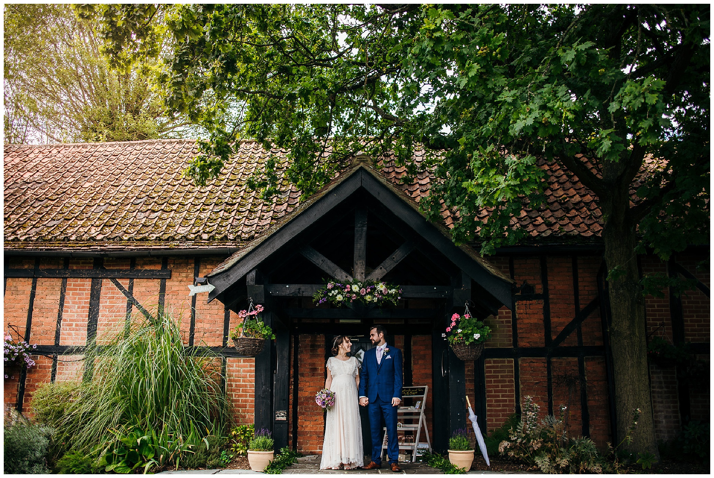 bride and groom stand hand in hand in front of tudor barn