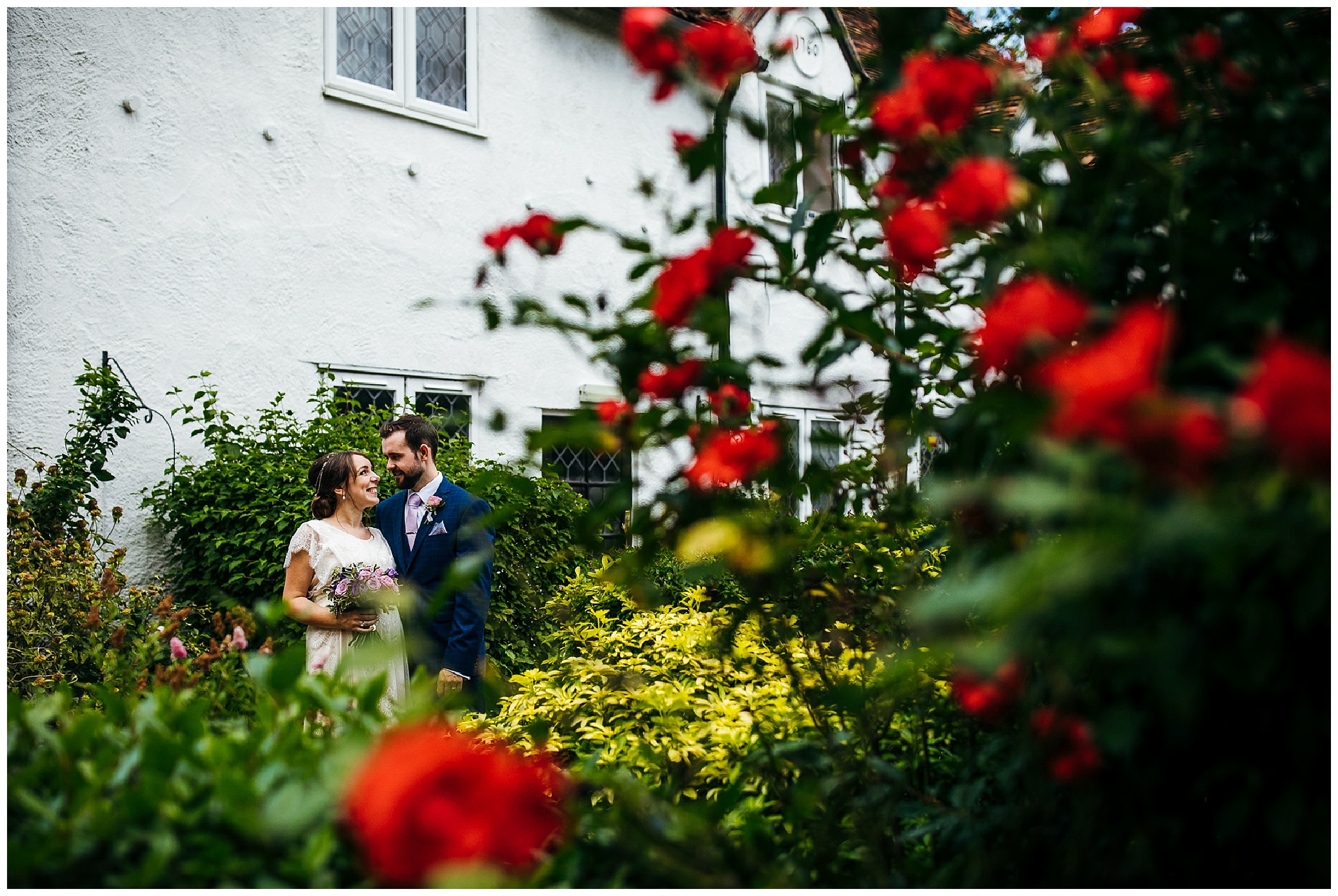 bride and groom in background with red roses in foreground