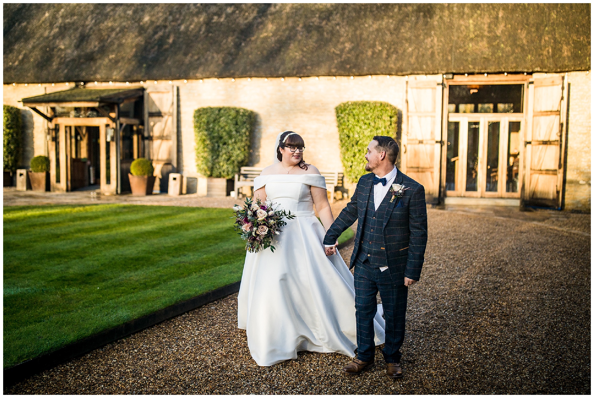 bride and groom walk hand in hand in front of tythe barn in launton