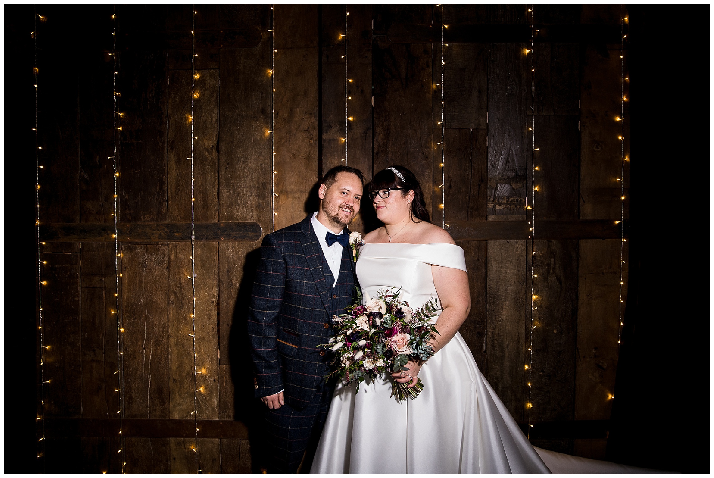 bride and groom in front of wall of fairy lights