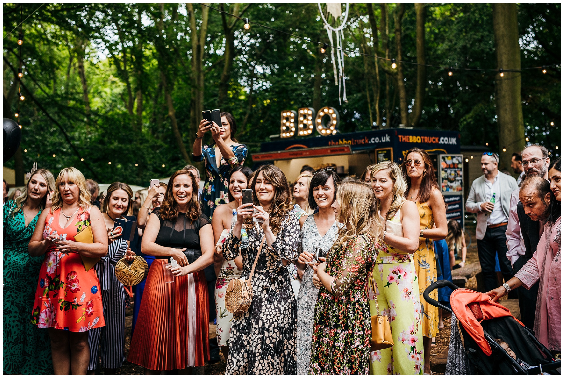 wedding guests scramble to take photos of happy couple at outdoor woodland wedding venue