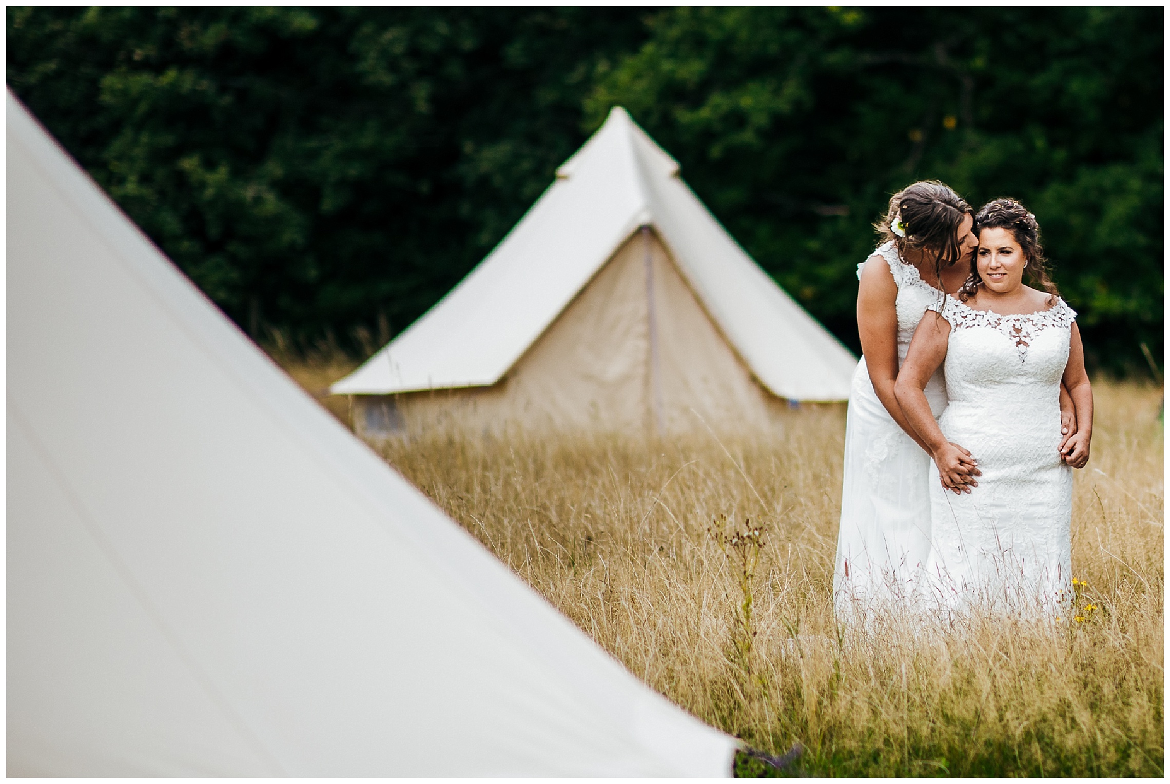 bride kisses bride on cheek around tipis