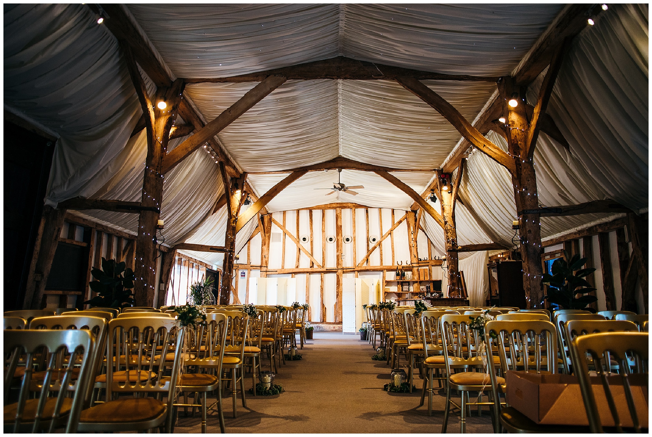 barn wedding venue with white drapes and open beams, gold chairs at south farm