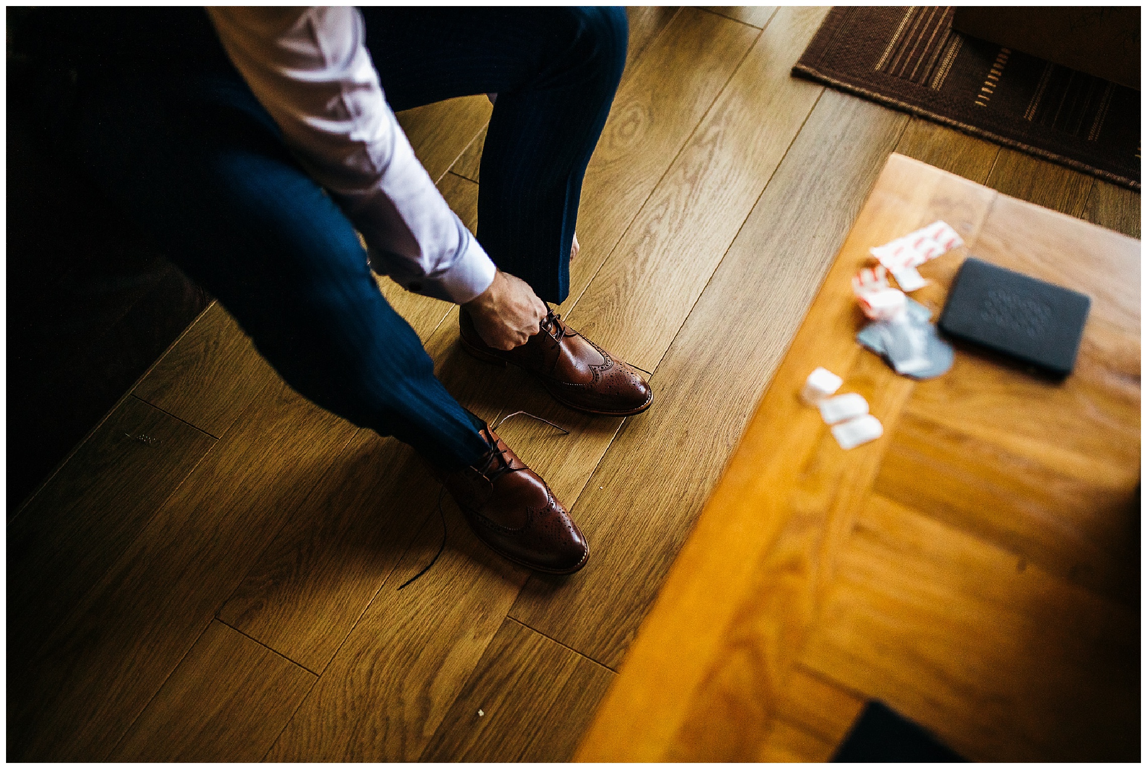 groom putting on brown leather shoes against wooden flooring