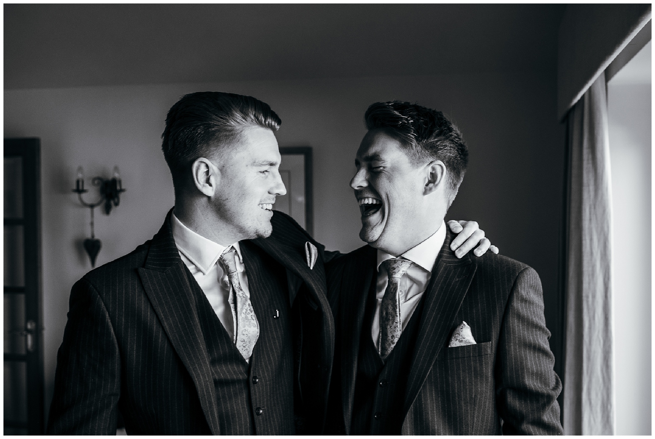 black and white image of groom and brother looking at each other laughing