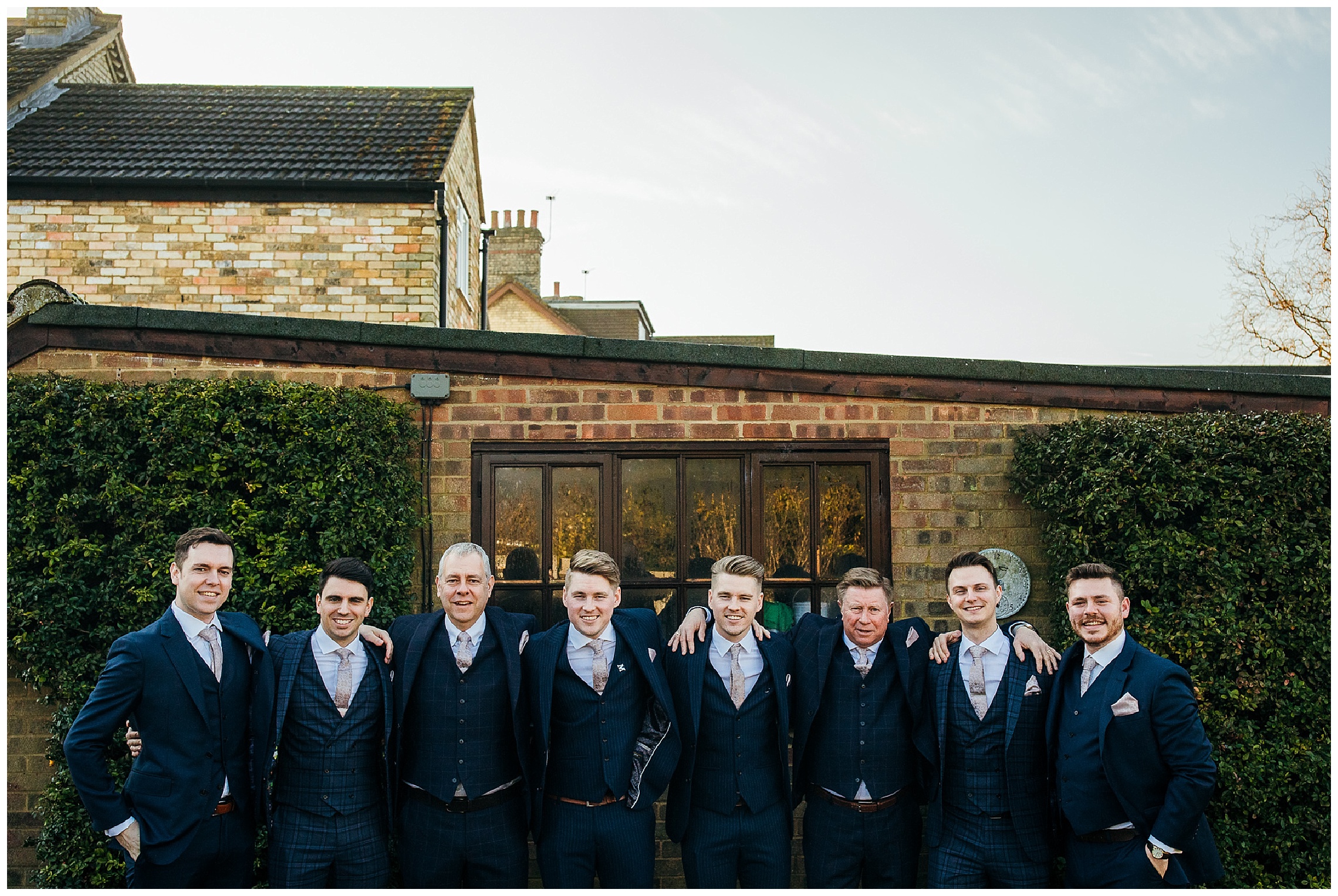 groomsmen in blue suits outside with arms around eachother smiling