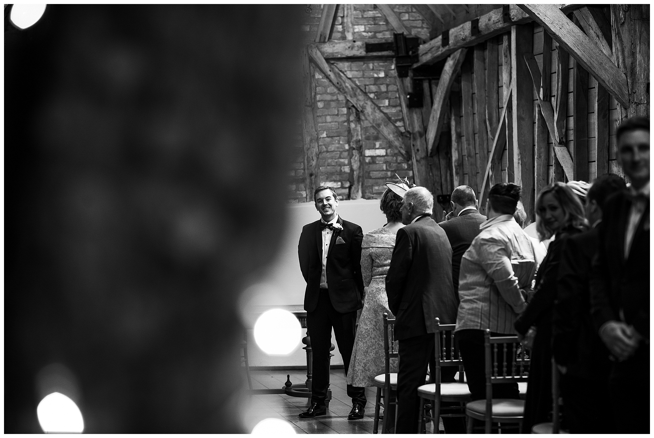 black and white image of groom waiting at end of aisle in rickety barn