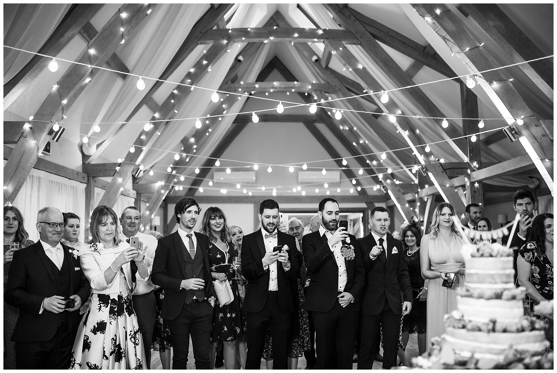 wedding guests taking photographs of bride and groom cutting wedding cake