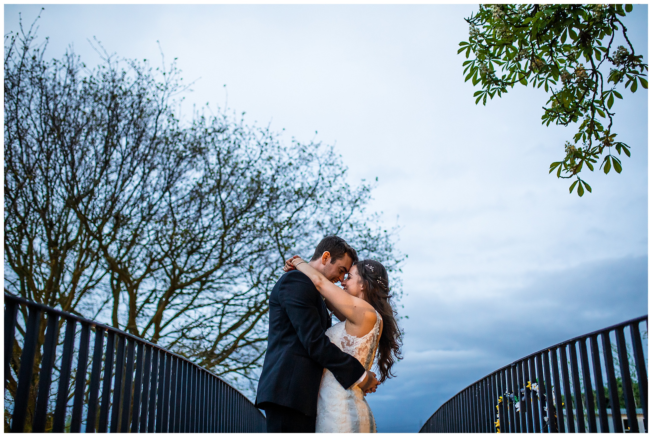 bride and groom stood together with arms around one another on blue bridge at bassmead manor barns