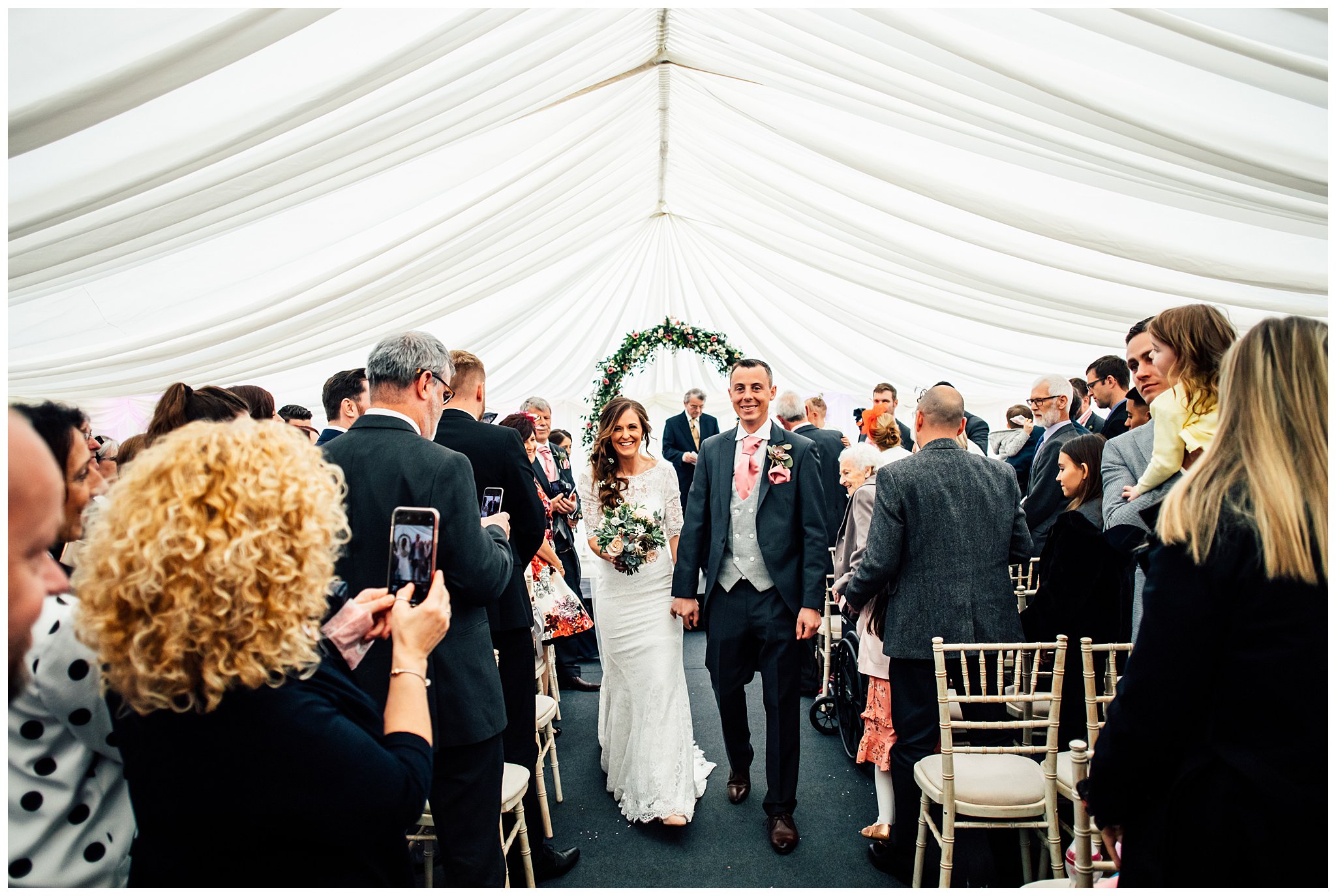 bride and groom walking down aisle hand in hand surrounded by large group of people